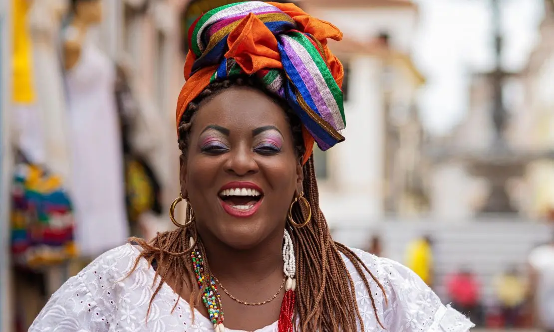 Baiana trajando roupas brancas com um lenço colorido e um sorriso no rosto