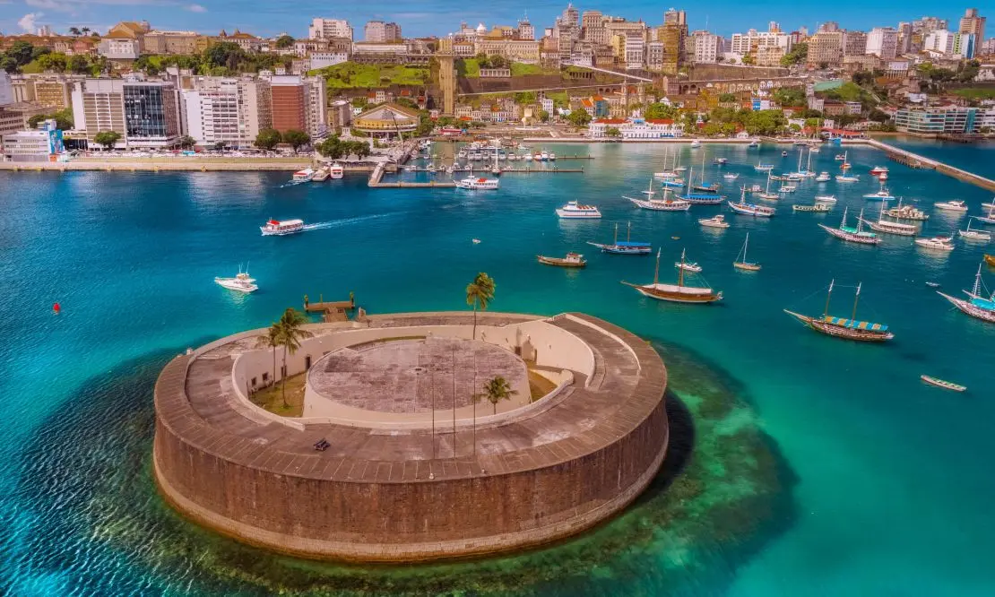 Forte em Salvador no meio do mar com a cidade ao fundo e barcos parados e ancorados no mar