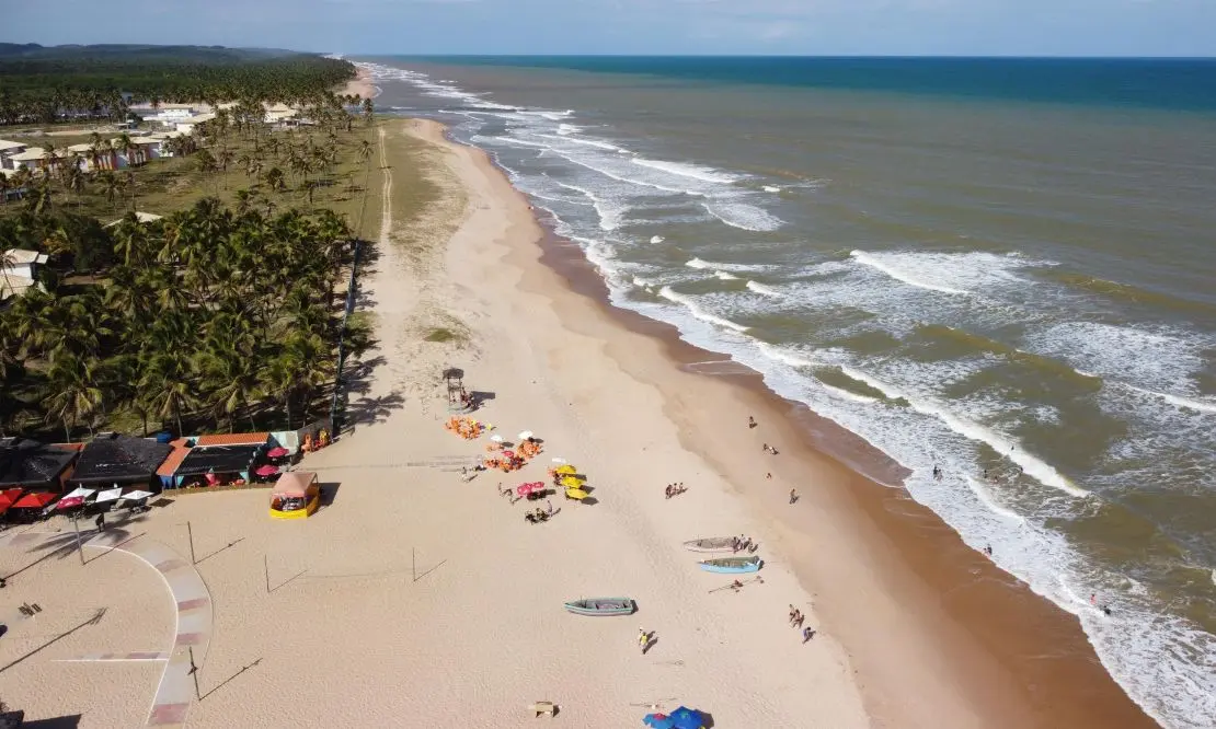 Vista aérea da orla da Praia de Baixio com pessoas, quiosques e caiaques parados na areia