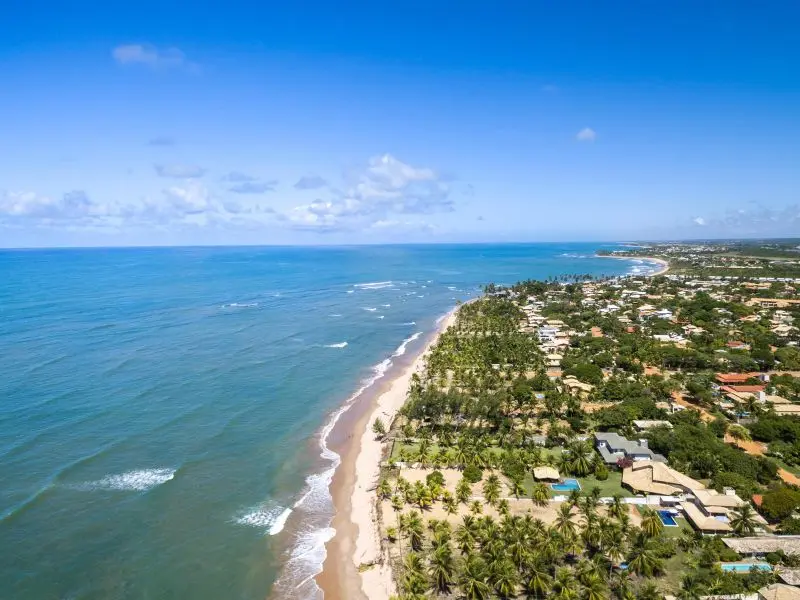 Orla da praia de Itacimirim, com as casas se misturando com a vegetação, enquanto o mar azul em contraste com a faixa de areia