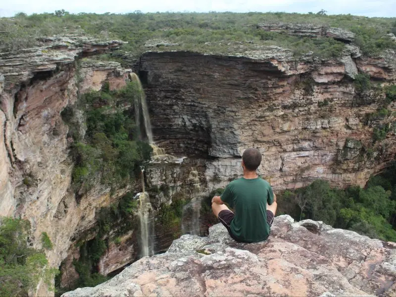 Homem sentado de pernas cruzadas na ponta de uma pedra, no topo do Morro do Chapéu