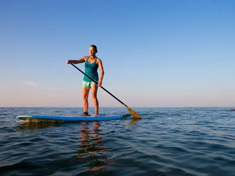 Mulher sobre uma prancha de SUP, remando em mar aberto