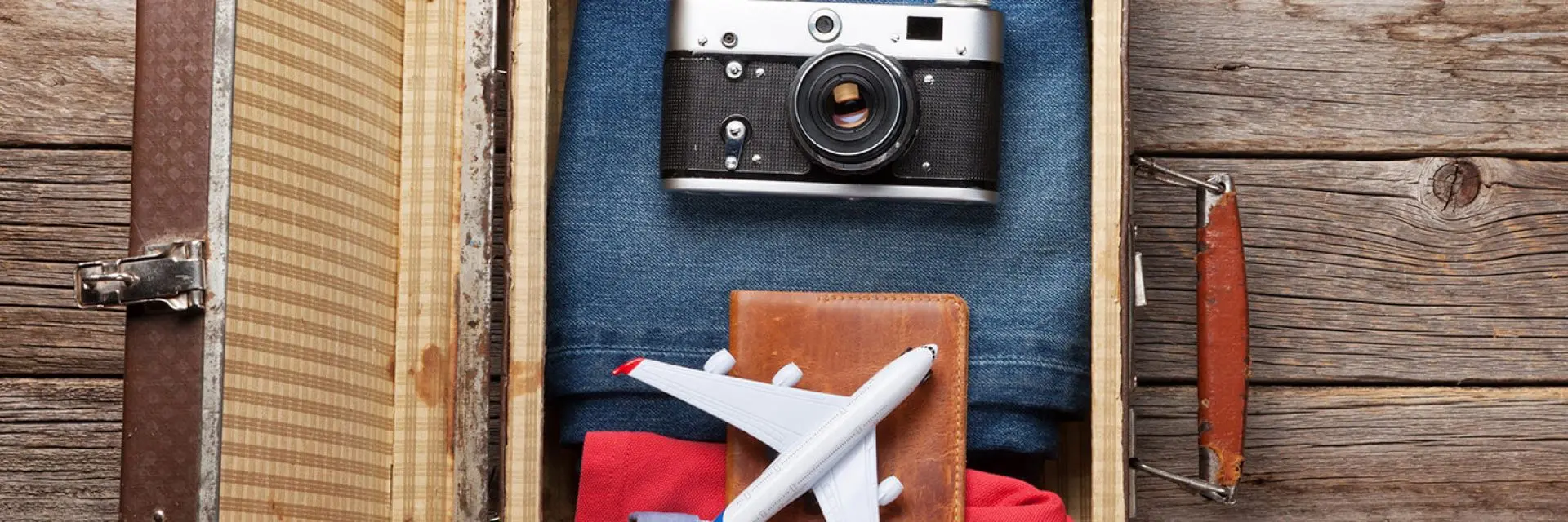 Imagem de uma mala de viagem com câmera, passaporte e um mini-avião