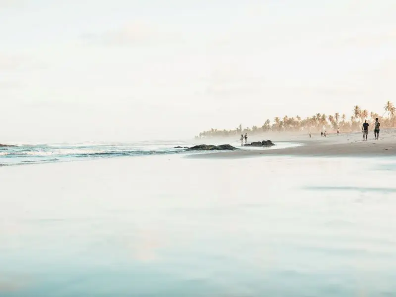 Imagem de uma praia com algumas pessoas andando na areia