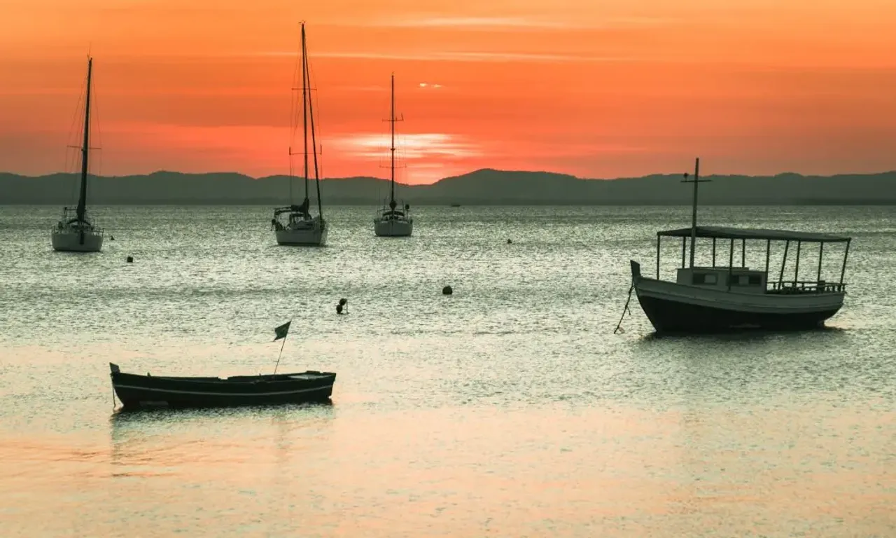 barcos ancorados proximos à praia de itaparica, com o pôr-do-sol no horizonte