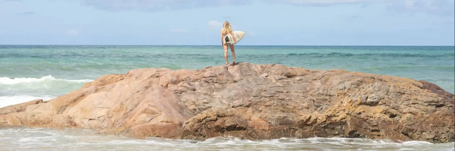 Imagem de uma pessoa com prancha em frente ao mar
