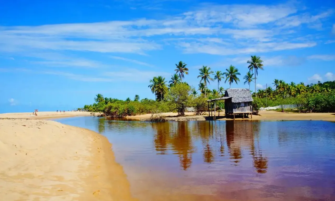 Afluente do rio entrando no mar e uma cabana de madeira perto da praia em Porto Seguro