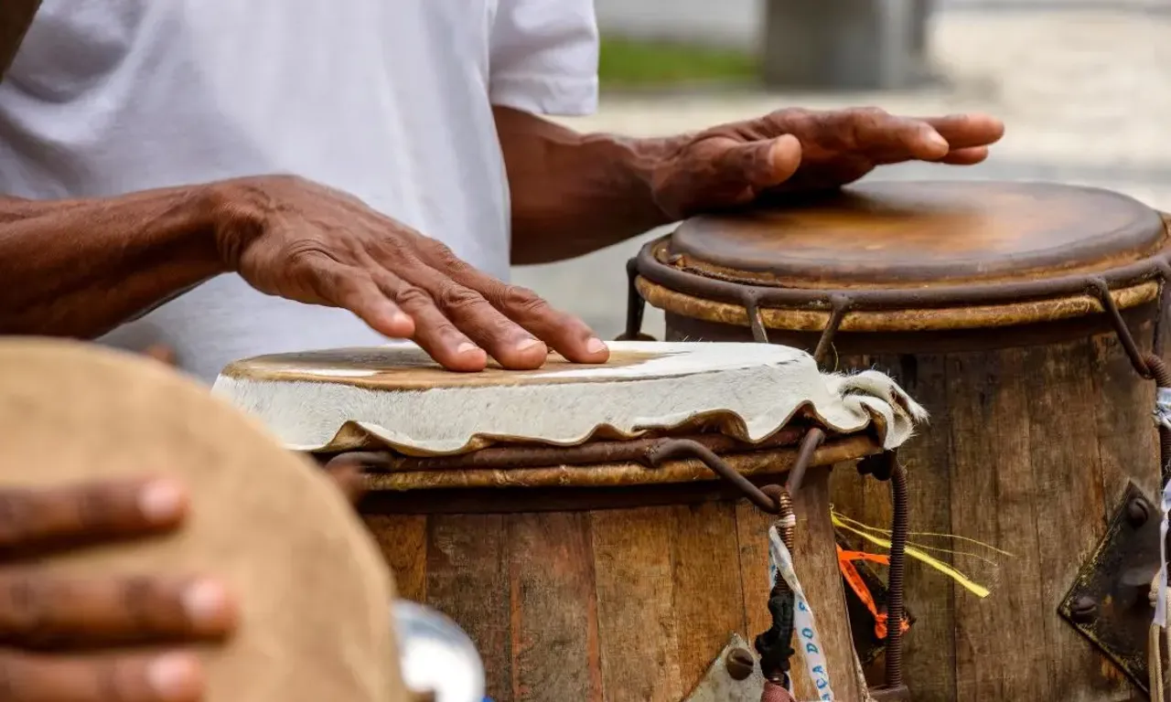 Parte das mãos de uma pessoa tocando atabaques em uma roda de Maculelê